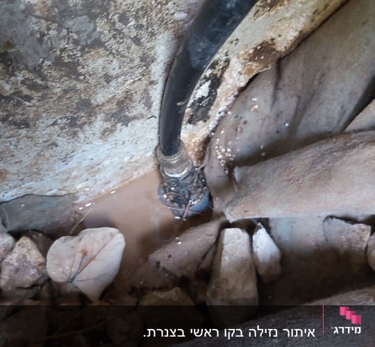צינור שחור דולף בין אבנים עם מים על הקרקע